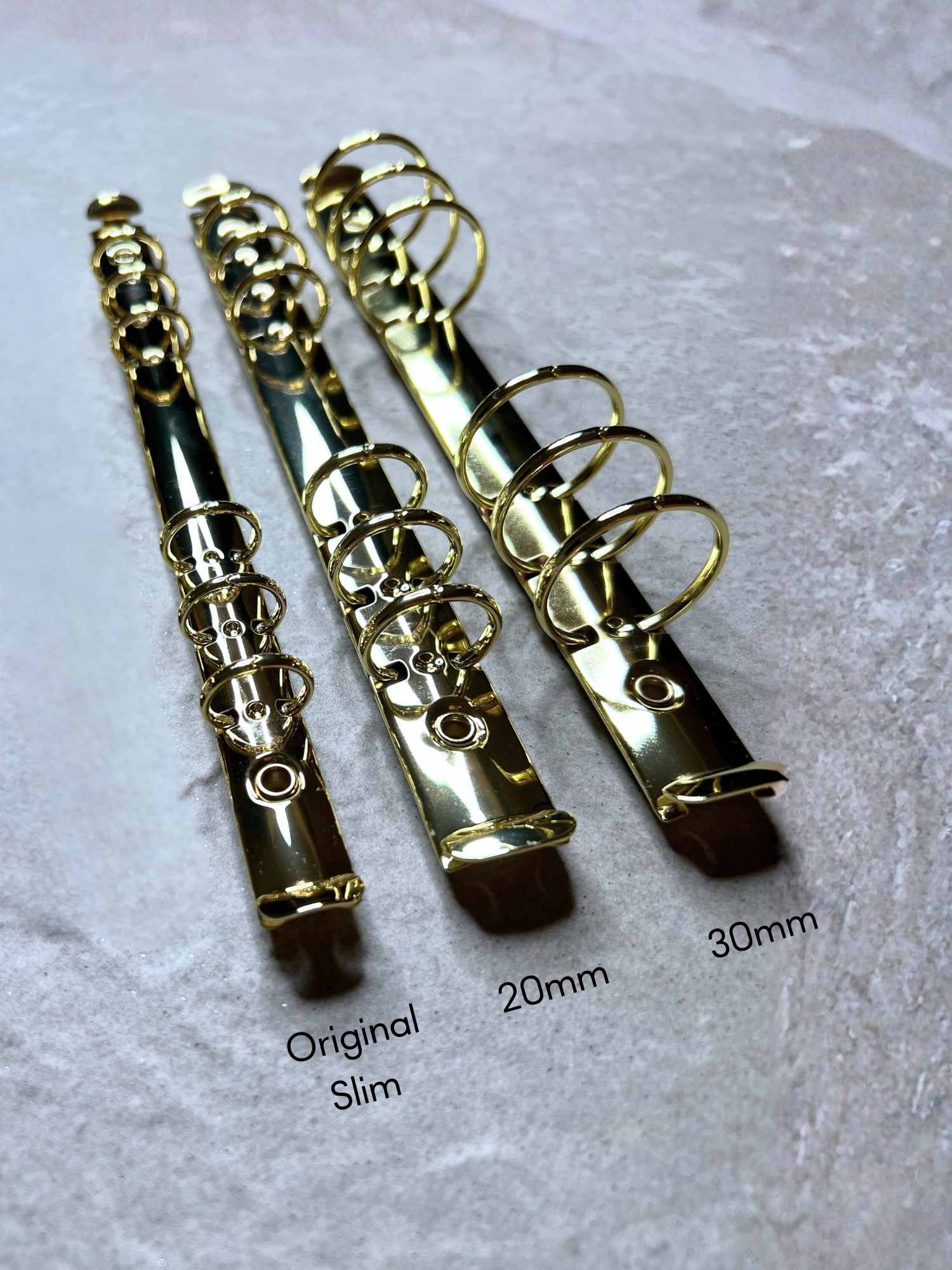 Three gold-colored binder clips on a textured gray background with size labels. by Pop In Planner from www.popinplanner.com